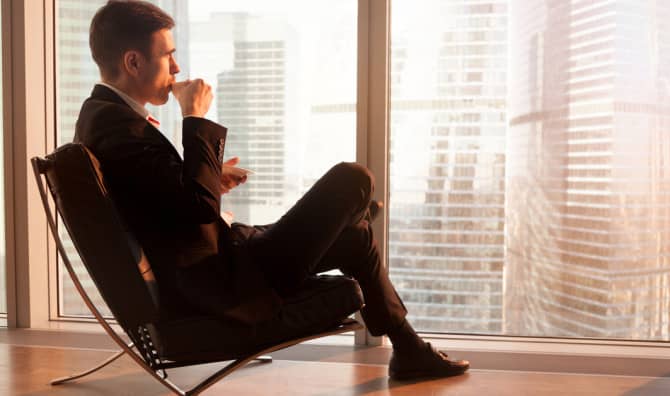 man sitting in chair watching city view from the window of a top floor