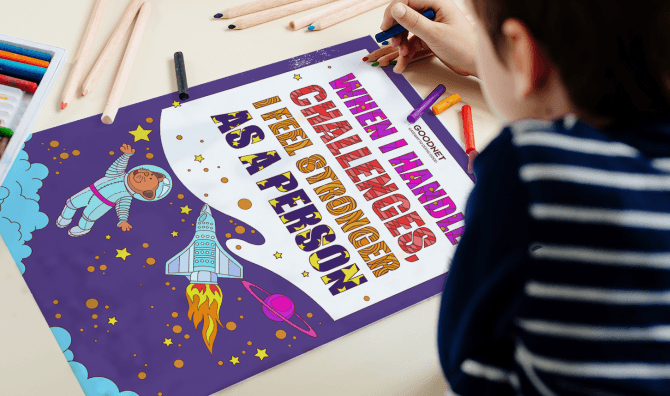 A child in a striped shirt seen from behind, coloring a space-themed motivational poster that reads 'When I handle challenges... I feel stronger as a person,' featuring illustrations of an astronaut, rocket ship, stars, and planets on a purple background, with crayons and colored pencils on the table.
