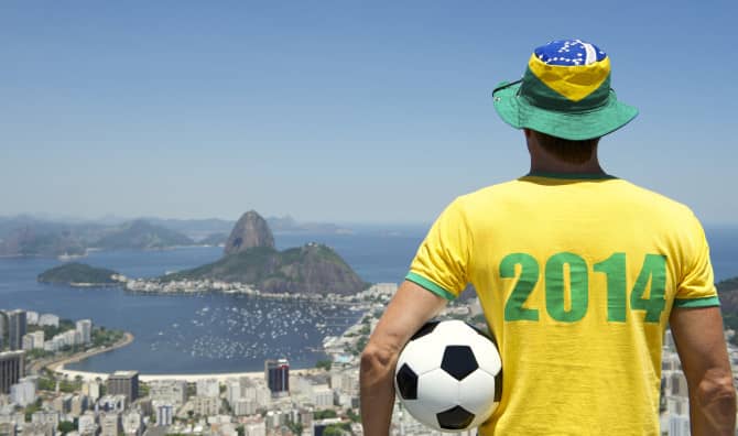 Man holding a soccer ball wearing a hat woth brazil flag colors watching a bay