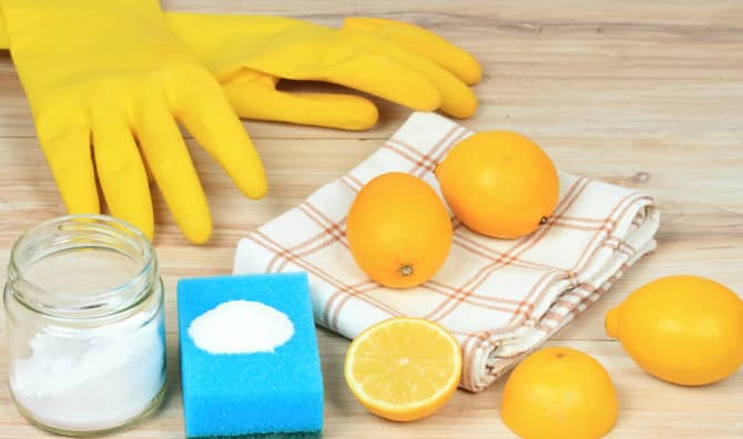 Natural cleaning supplies: lemons, baking soda, a blue sponge, yellow rubber gloves, and a checkered cloth on a wooden surface.