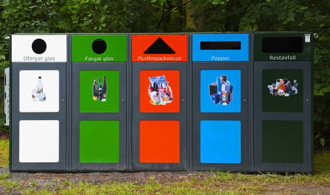 Five colored waste separation bins lined up outdoors - white, green, orange, blue, and dark gray containers.