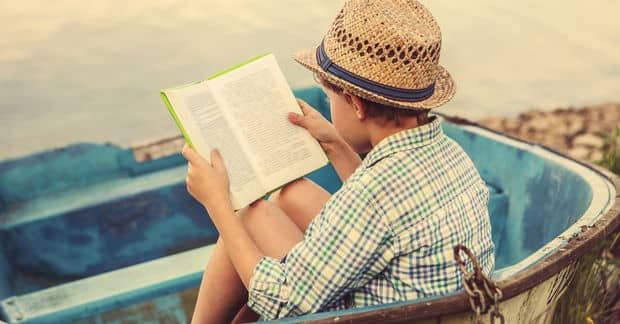 Boy sitting in a boat on a shore reading a book
