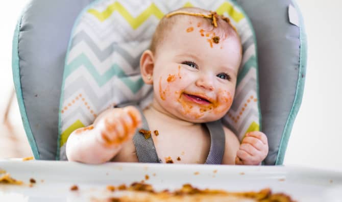 Happy messy baby in high chair after eating.