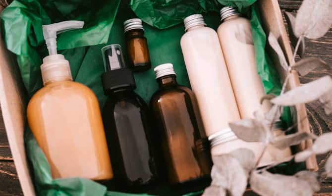 Assorted skincare bottles in various sizes and colors nestled in green tissue paper inside a cardboard gift box.