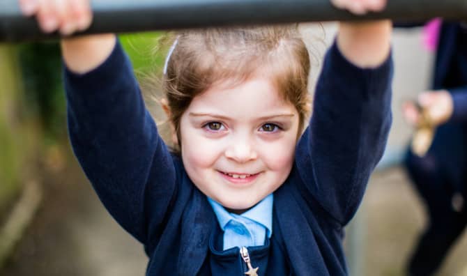 Young girl in school uniform celebrating with raised arms.