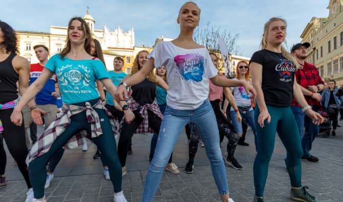 A group of young women perform a synchronized dance routine together in a city square on a sunny day.