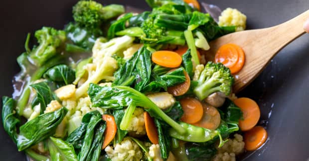 Fresh vegetables stir-frying in wok with wooden spoon.