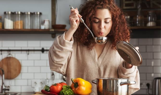 A woman boiling vegetables to make soup.