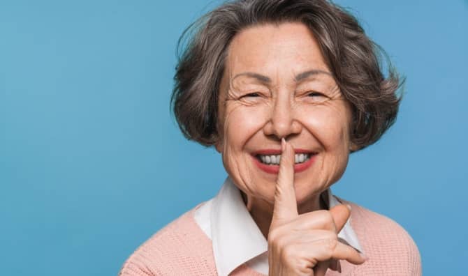 A smiling woman holds her finger to her lips, signaling for quiet.