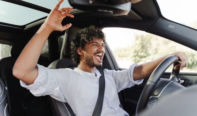 A young man happily drives while singing to music.