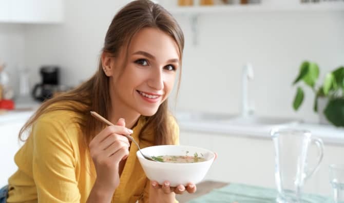 A woman eating hot chicken soup.