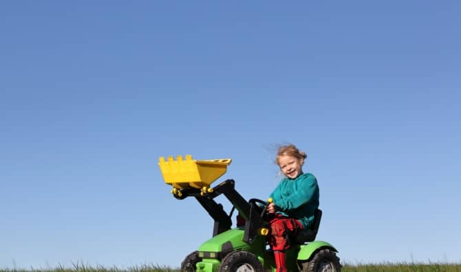 A happy young girl plays on a toy tractor.