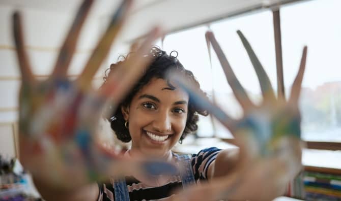 A woman smiles with colorful painted hands.