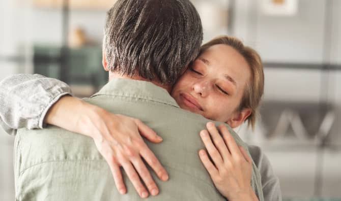 An adult daughter hugs her father.