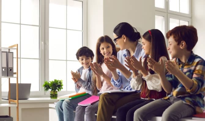 A female teacher claps together with a group of happy children.