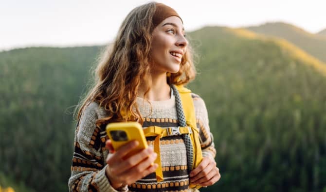 A woman walks in nature while holding her phone.