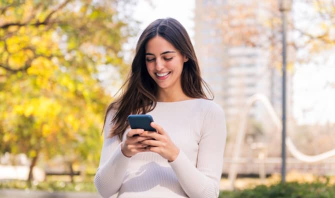 A woman smiles while she uses her phone.