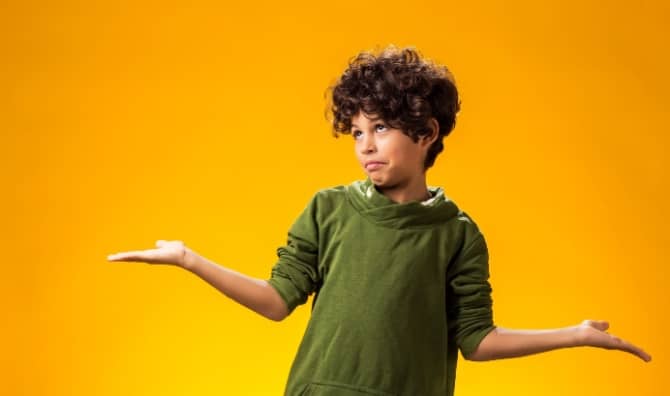 A boy keeps his arms to the side and shrugs.