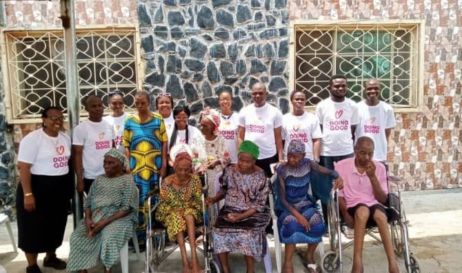Good Deeds Day volunteers in Nigeria stand behind elderly residents seated outdoors.
