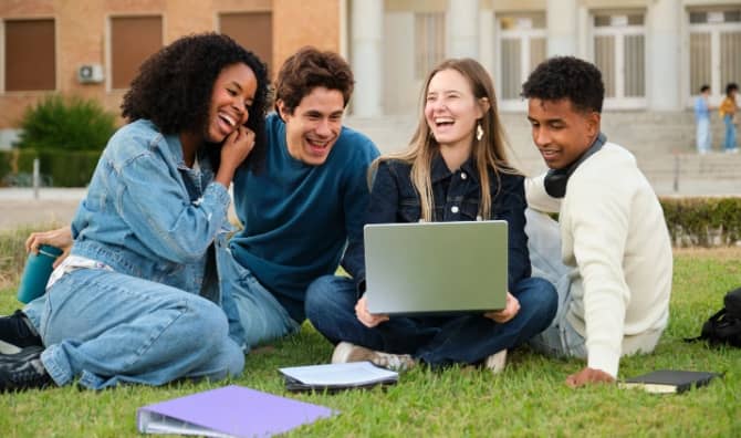 A diverse group of young adults sitting on the grass and smiling.