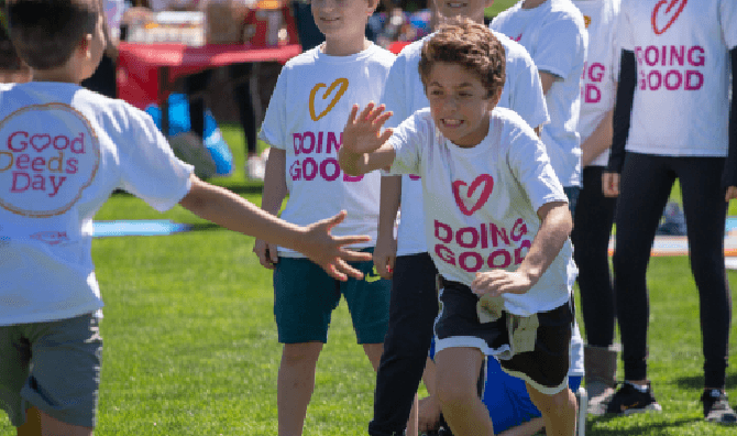 Children wearing “Doing Good” shirts run and play together at a community event.