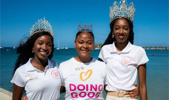 Three women wearing tiaras and Good Deeds Day shirts stand by the water.