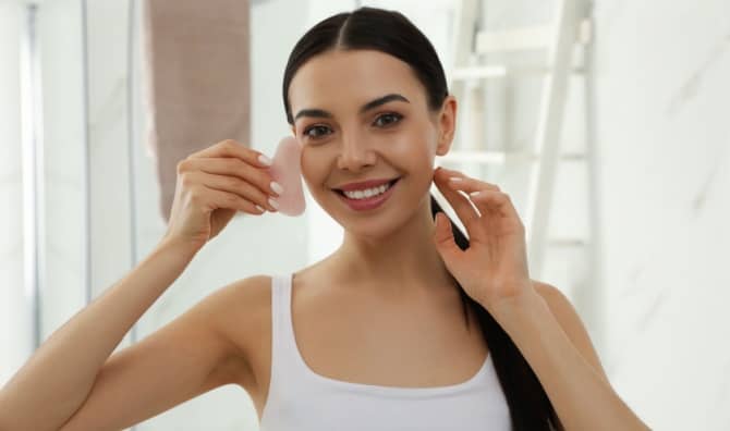 A woman does a facial massage with a gua sha tool.