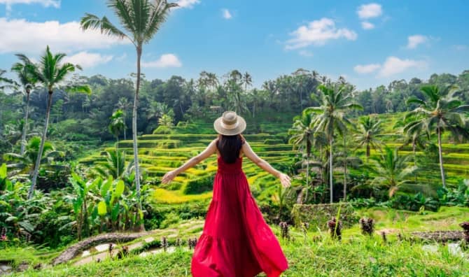 A female tourist in a red dress looks at a rice terrace in Bali, Indonesia.