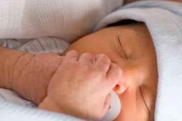 Newborn preemie holds his white pacifier.