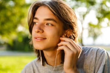 Cheerful older teen listening to a language app on his mobile phone.