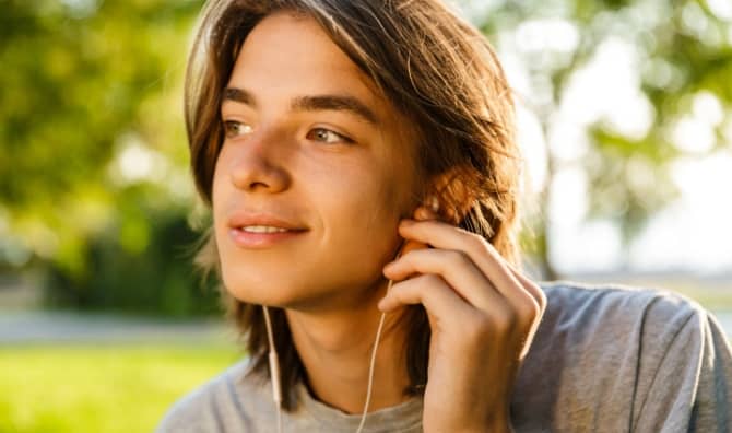 Cheerful older teen listening to a language app on his mobile phone.