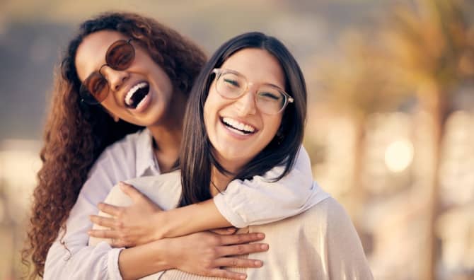 Two smiling friends embracing outdoors and laughing together.