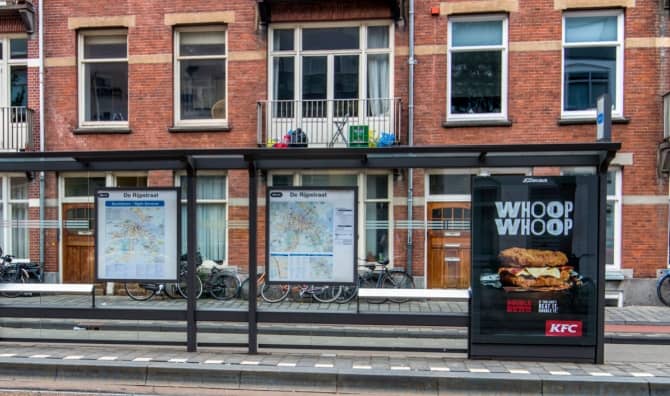 An Amsterdam tram stop with a fast-food advertisement.