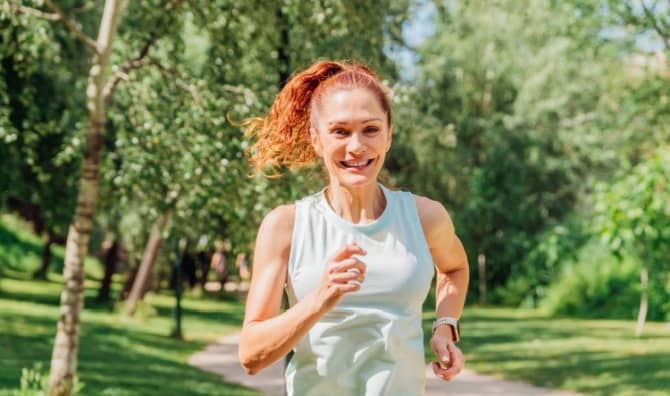 A smiling woman running through a vibrant city park.