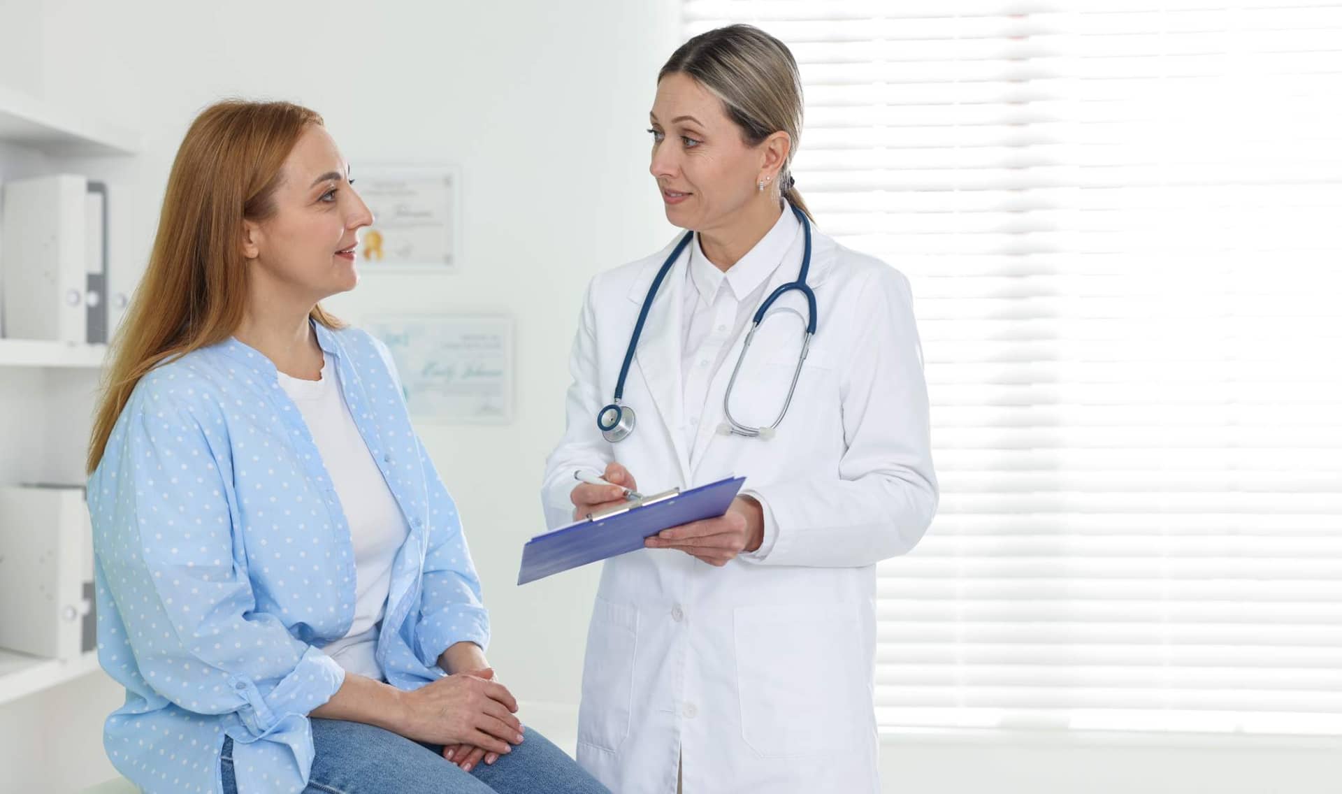 A smiling doctor with a clipboard consulting a patient in a clinic.