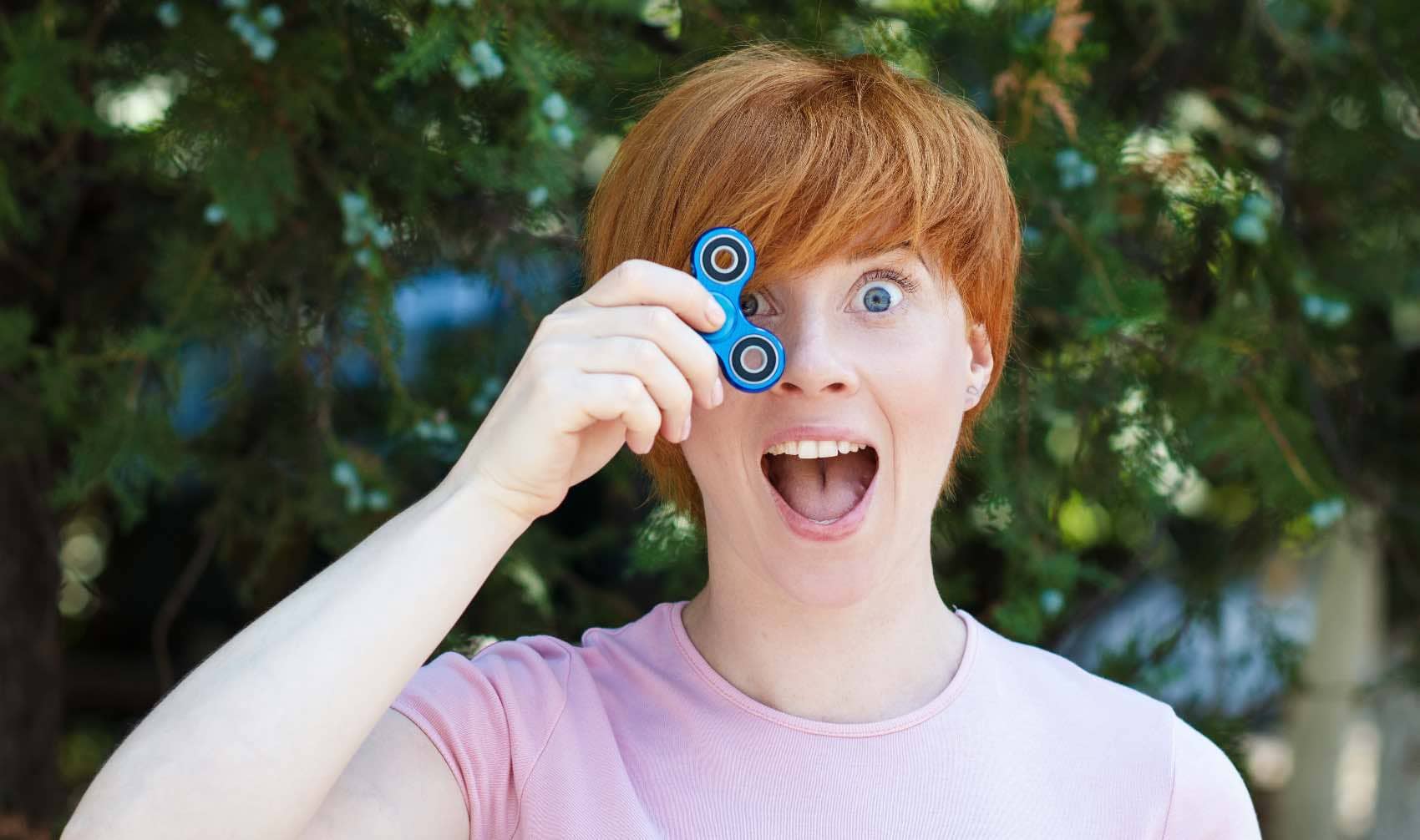 A smiling woman in a pink t-shirt holding a blue fidget spinner.