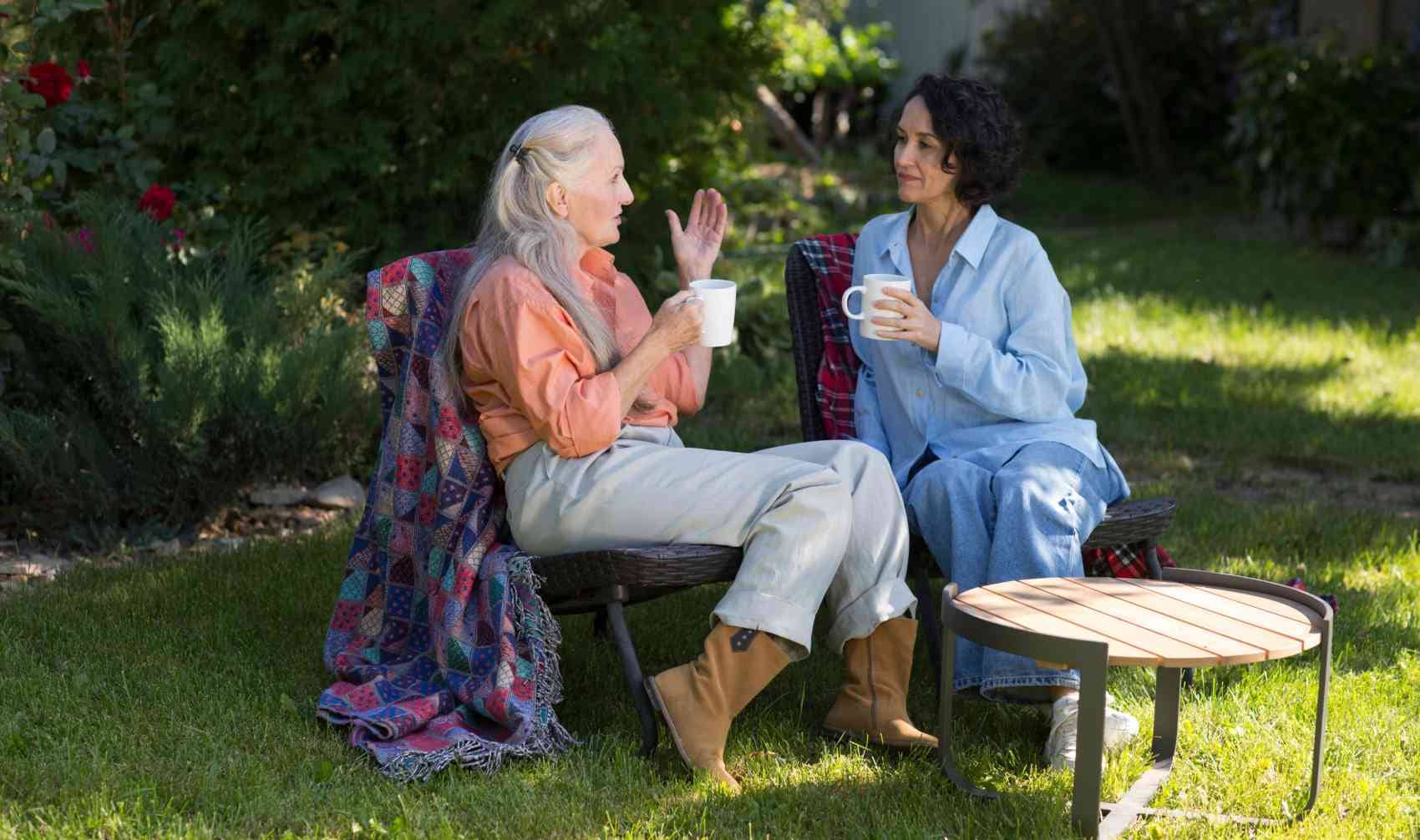 Two female friends drink tea and talk while sitting on chairs in a summer garden.