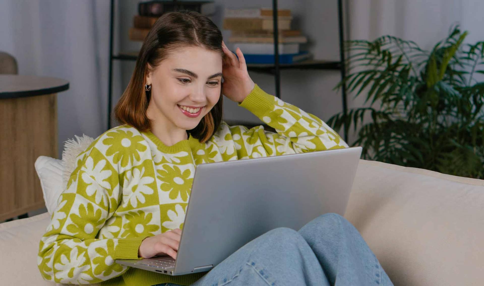 A smiling woman using a laptop while sitting on a couch.
