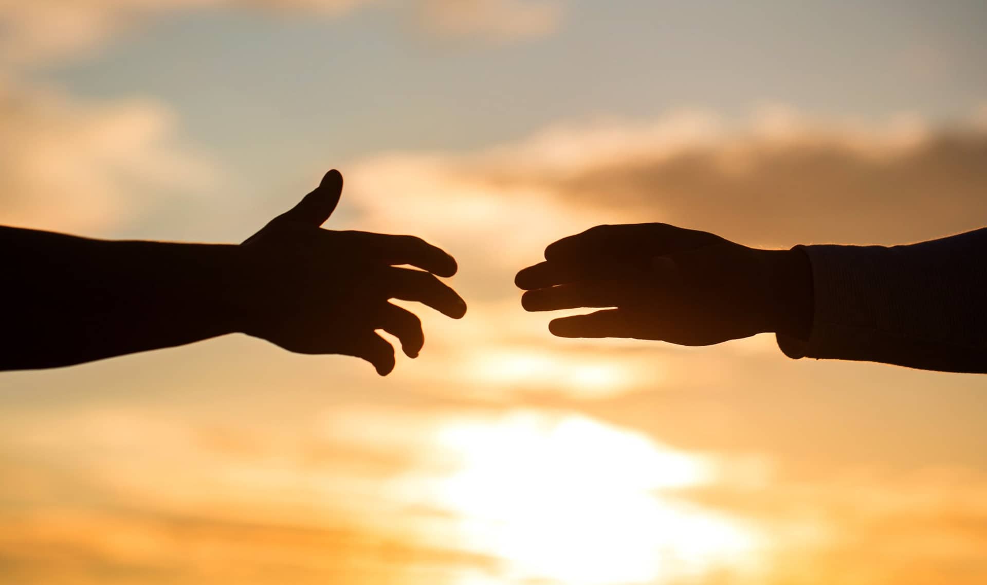 Two silhouetted hands reach toward each other against a golden sky.