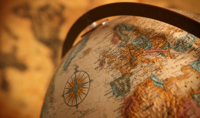 Close-up of a vintage antique globe with a metal band showing continents, ocean labels, and a compass rose design on the surface.
