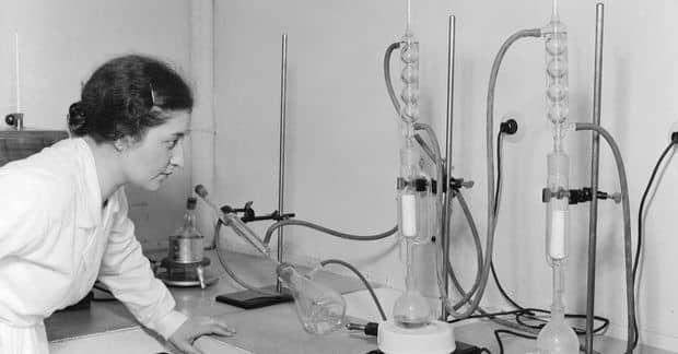 Wonan in white shirt and tie conducting a scientific experiment with laboratory equipment and glass apparatus in a black and white photograph