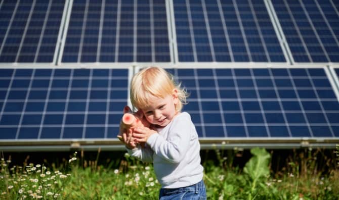 Child playing with a piggy bank in front of solar panels.