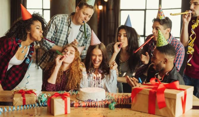 A group of friends celebrate together around a cake.
