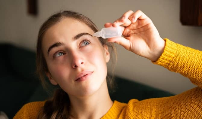A woman using eye drops in a living room.