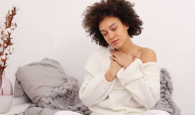 A woman sits with her hands on her chest.