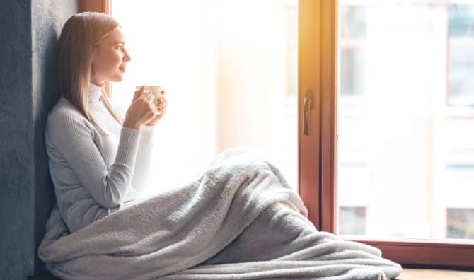 A woman sits by a window and holds a cup.
