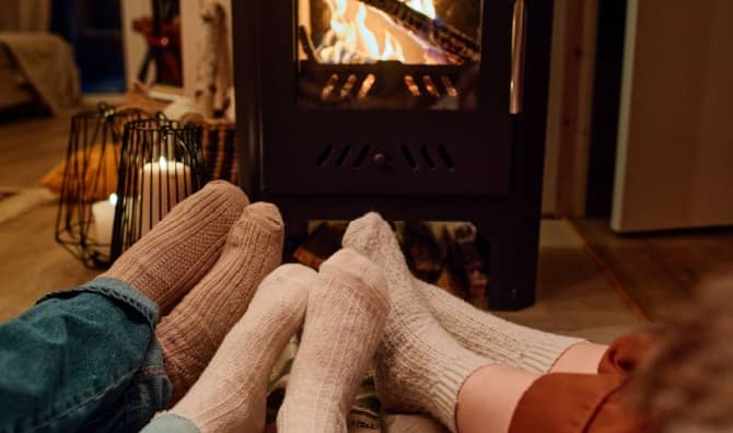 Three people wearing cozy socks sit together on the floor in front of a fireplace in a home.