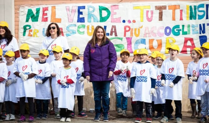 Shari Arison stands with a group of children wearing “Doing Good” shirts.