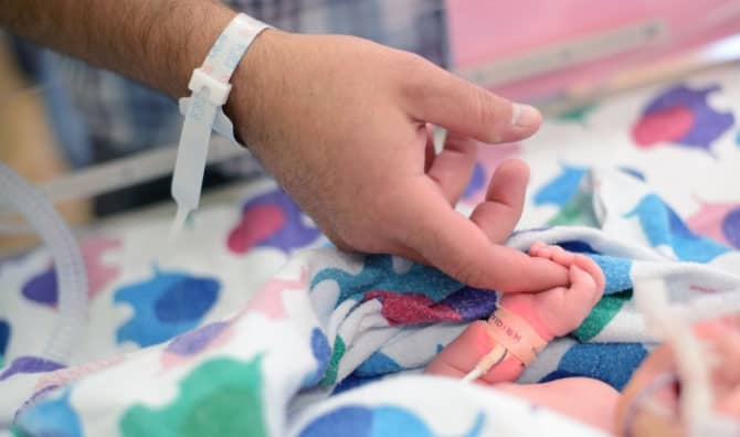 A first-time dad holds the tiny finger of his newborn who needed a little help breathing so was in the NICU.