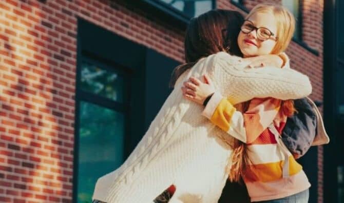 A mother kneels down to hug her daughter.